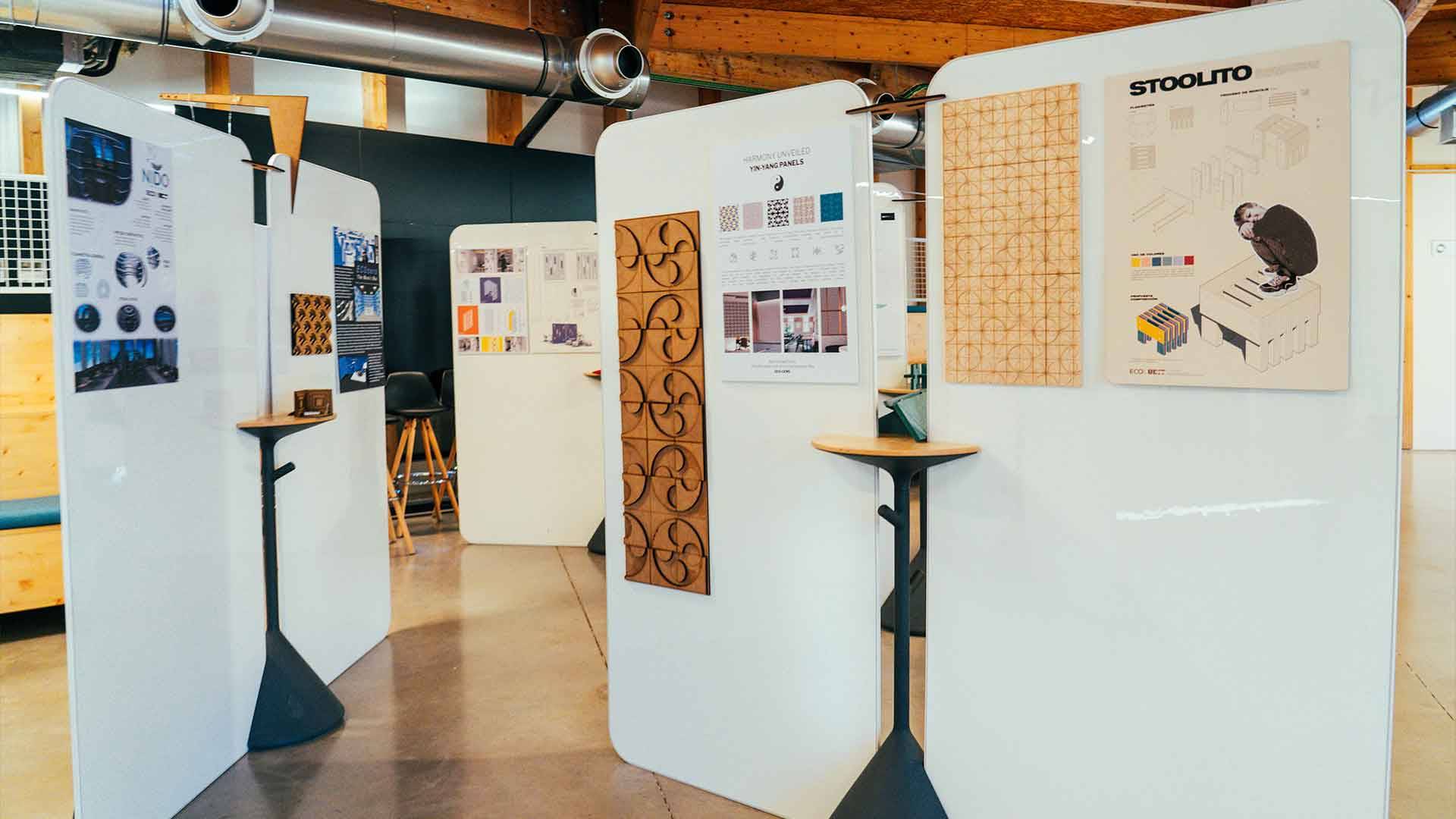 La imagen muestra un ambiente de exposición con paneles que exhiben diversos diseños y proyectos creativos.