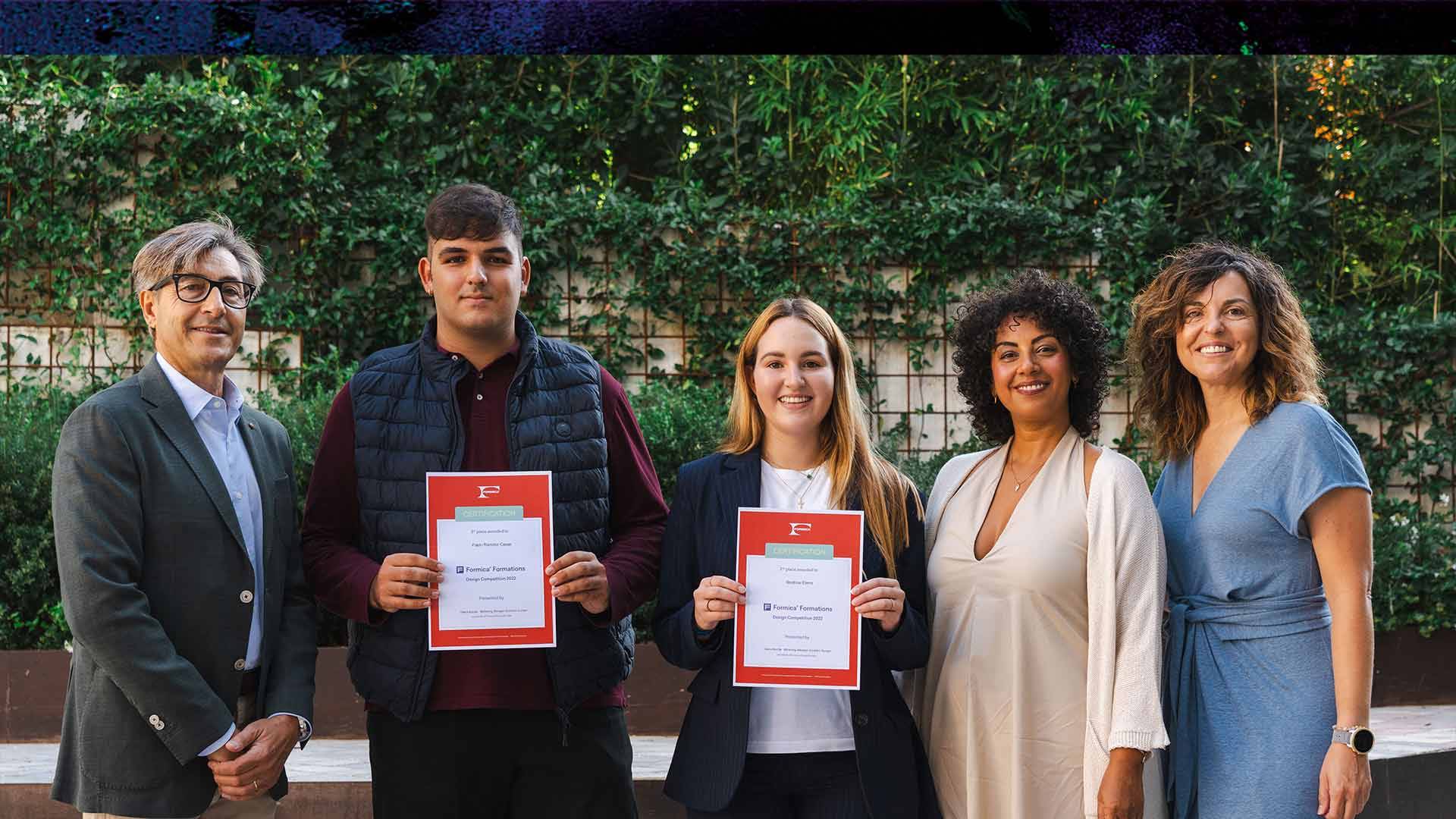 Un grupo de cinco personas se encuentra posando con diplomas en un entorno al aire libre.