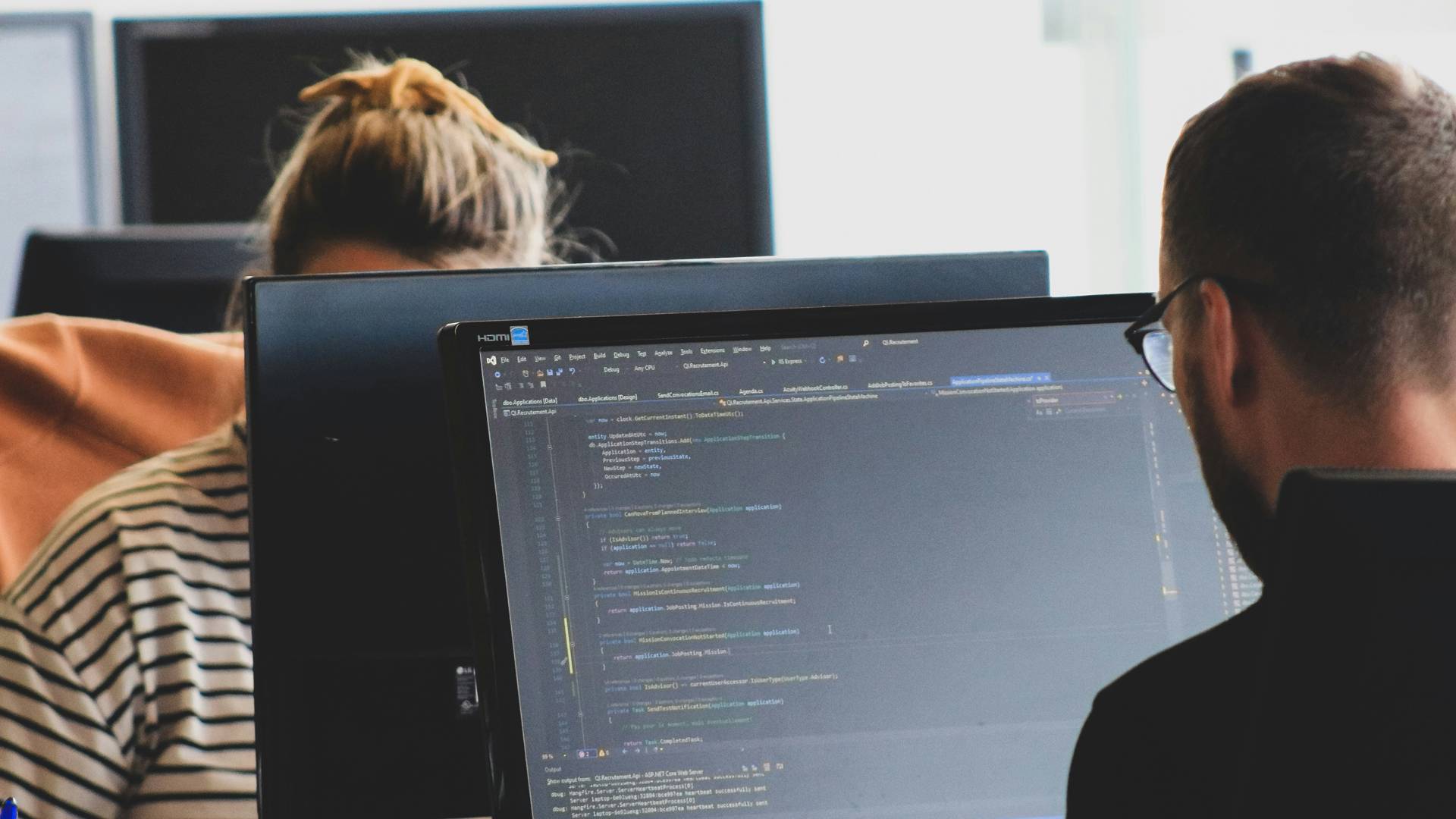 Dos personas trabajando en computadoras, una de ellas enfocada en escribir código.