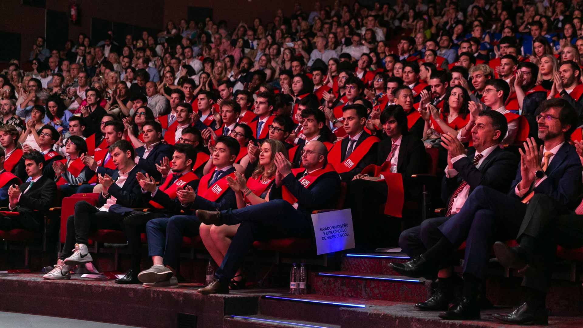 Un grupo de graduados en un auditorio aplaudiendo con entusiasmo.