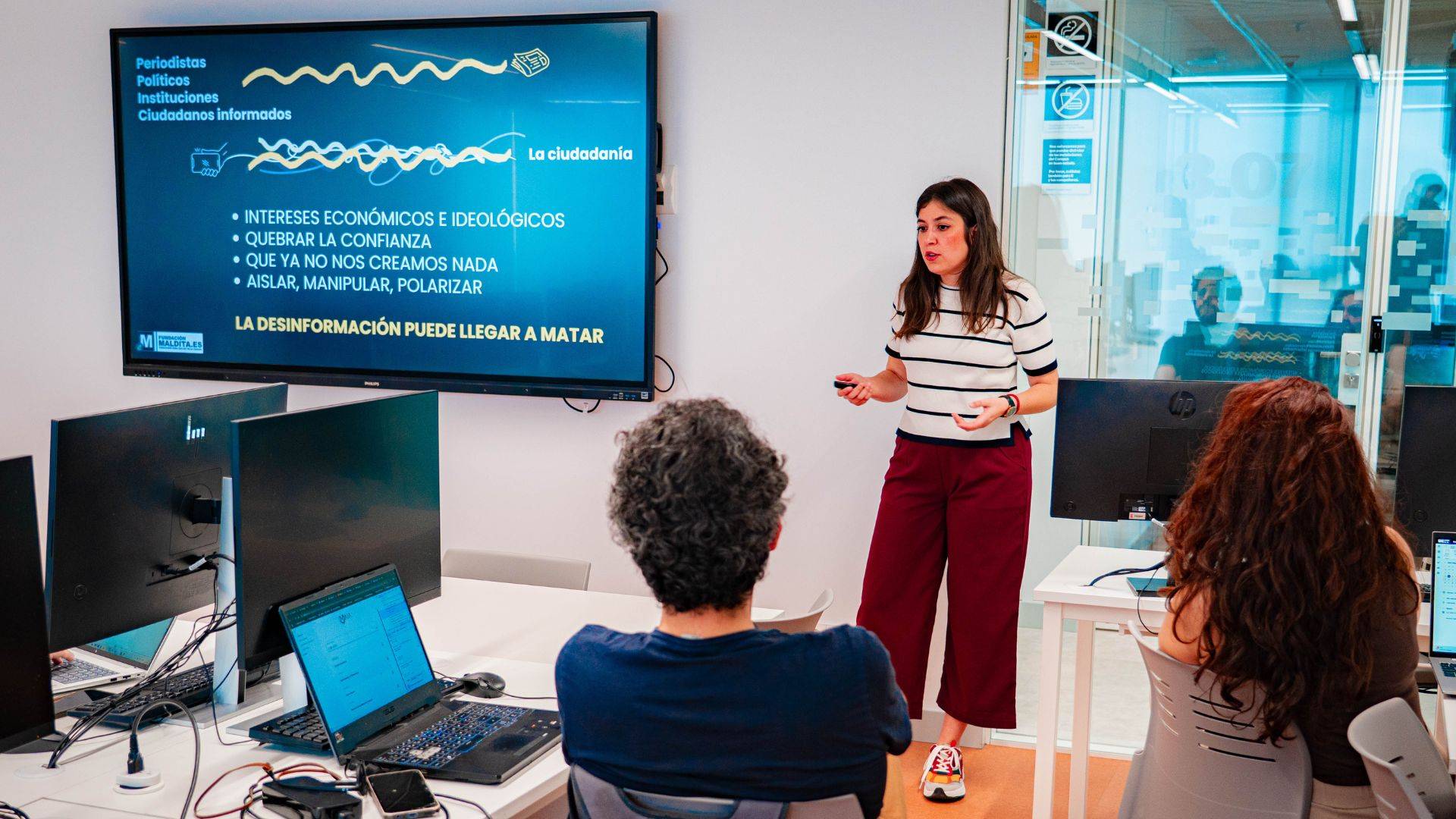 Una presentadora expone sobre la desinformación y sus riesgos frente a un grupo de asistentes en un aula.