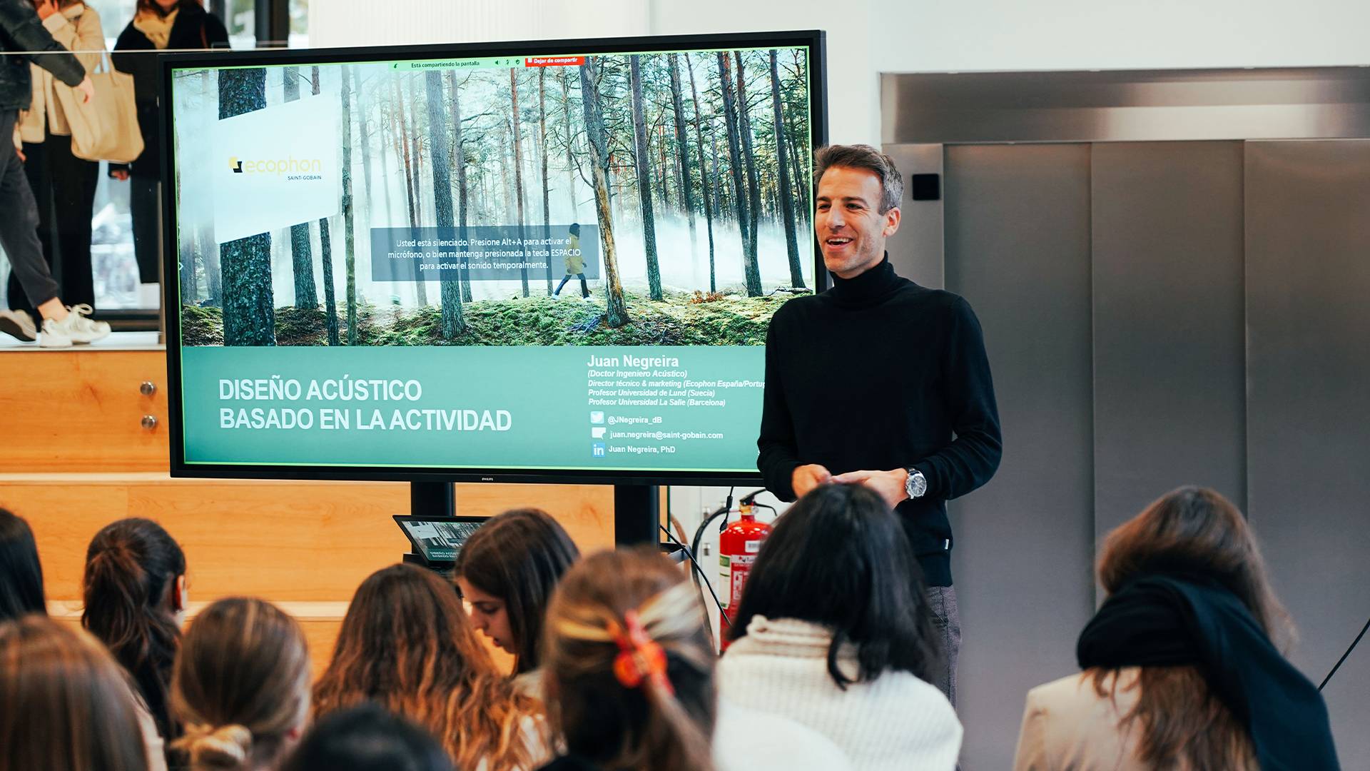 Un presentador habla sobre diseño acústico frente a una audiencia en un ambiente académico.