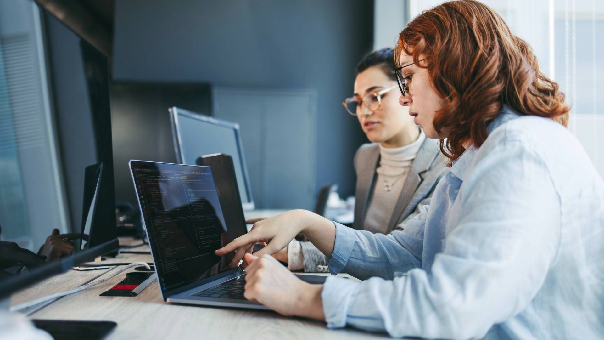 Dos mujeres trabajan juntas en un ordenador portátil en una oficina moderna.