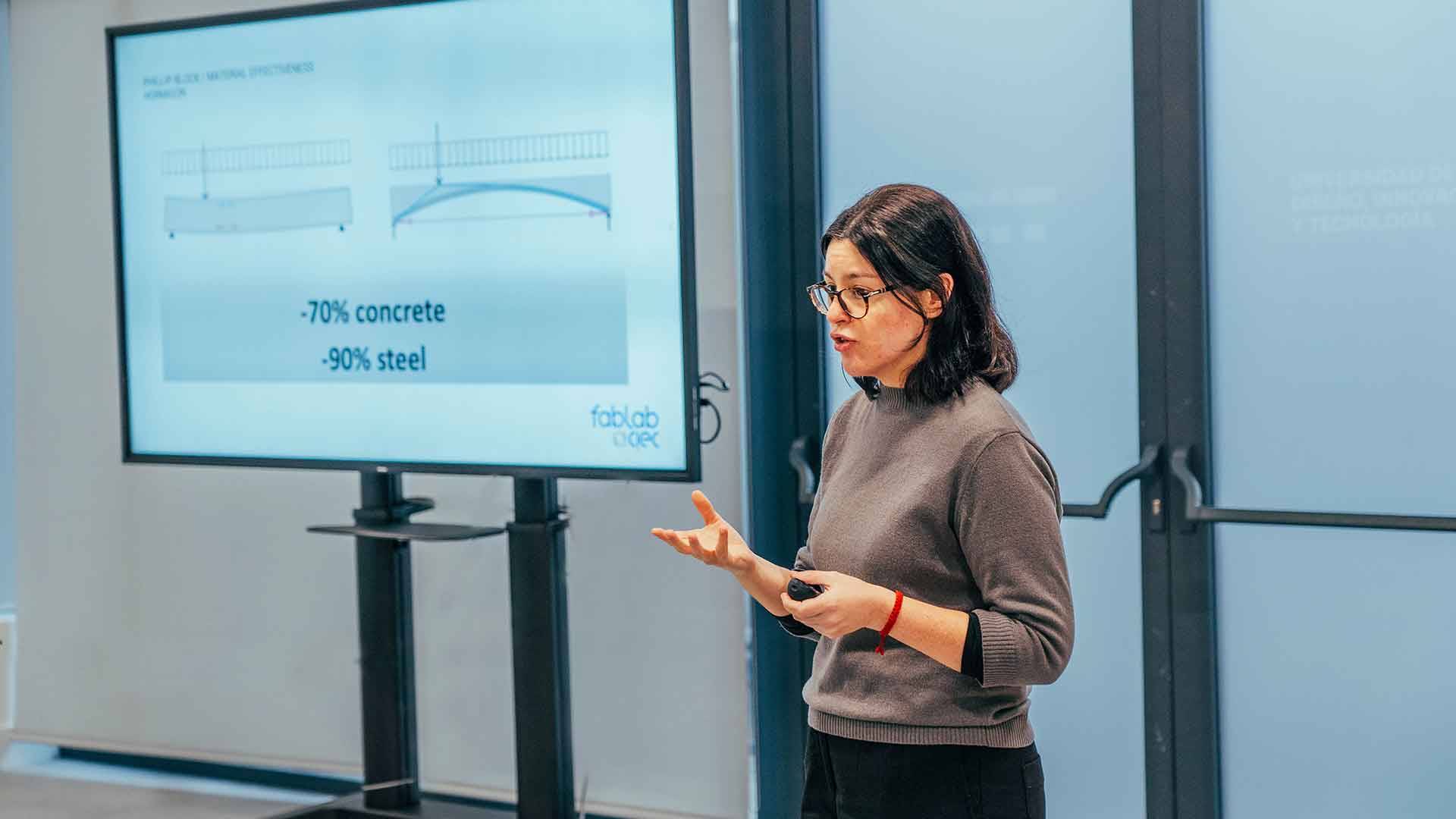 Una mujer está dando una presentación frente a una pantalla que muestra diagramas estructurales.