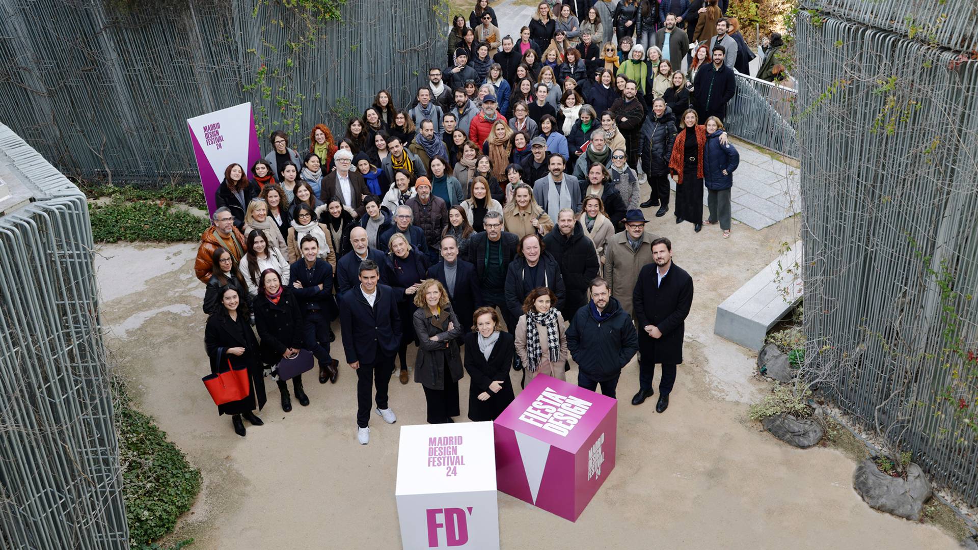 Un gran grupo de personas se reúne en un evento al aire libre con cajas de colores visibles en el primer plano.