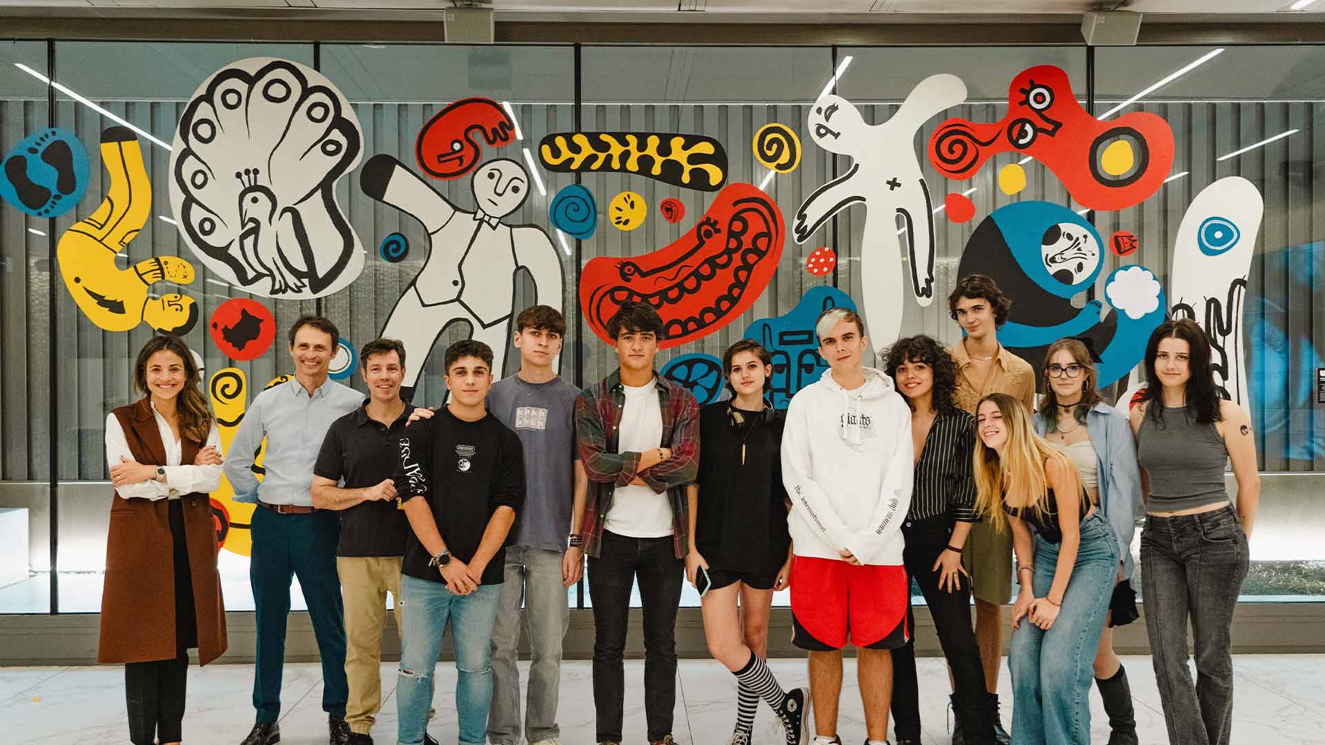 Un grupo de jóvenes posando frente a un mural colorido en un espacio interior moderno.