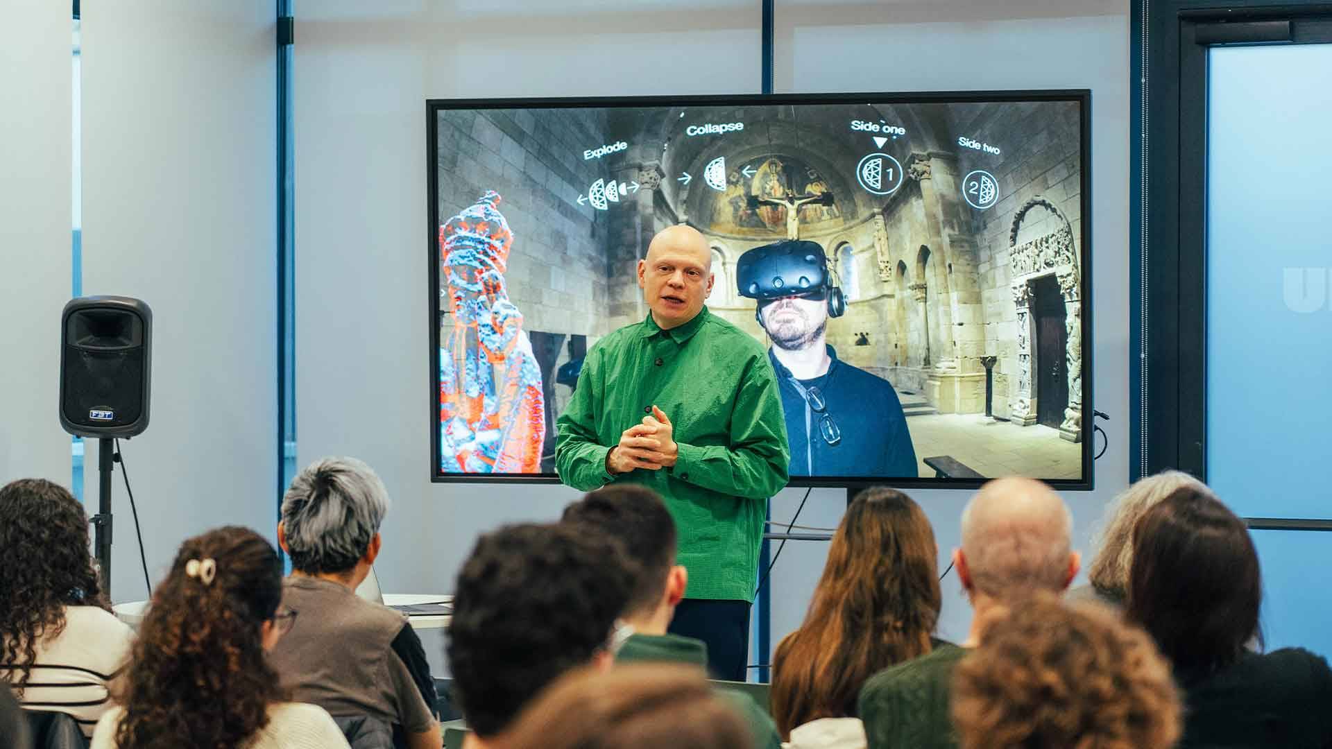 Una presentación interactiva en un evento con un ponente que habla frente a un auditorio y una pantalla detrás mostrando contenido visual.