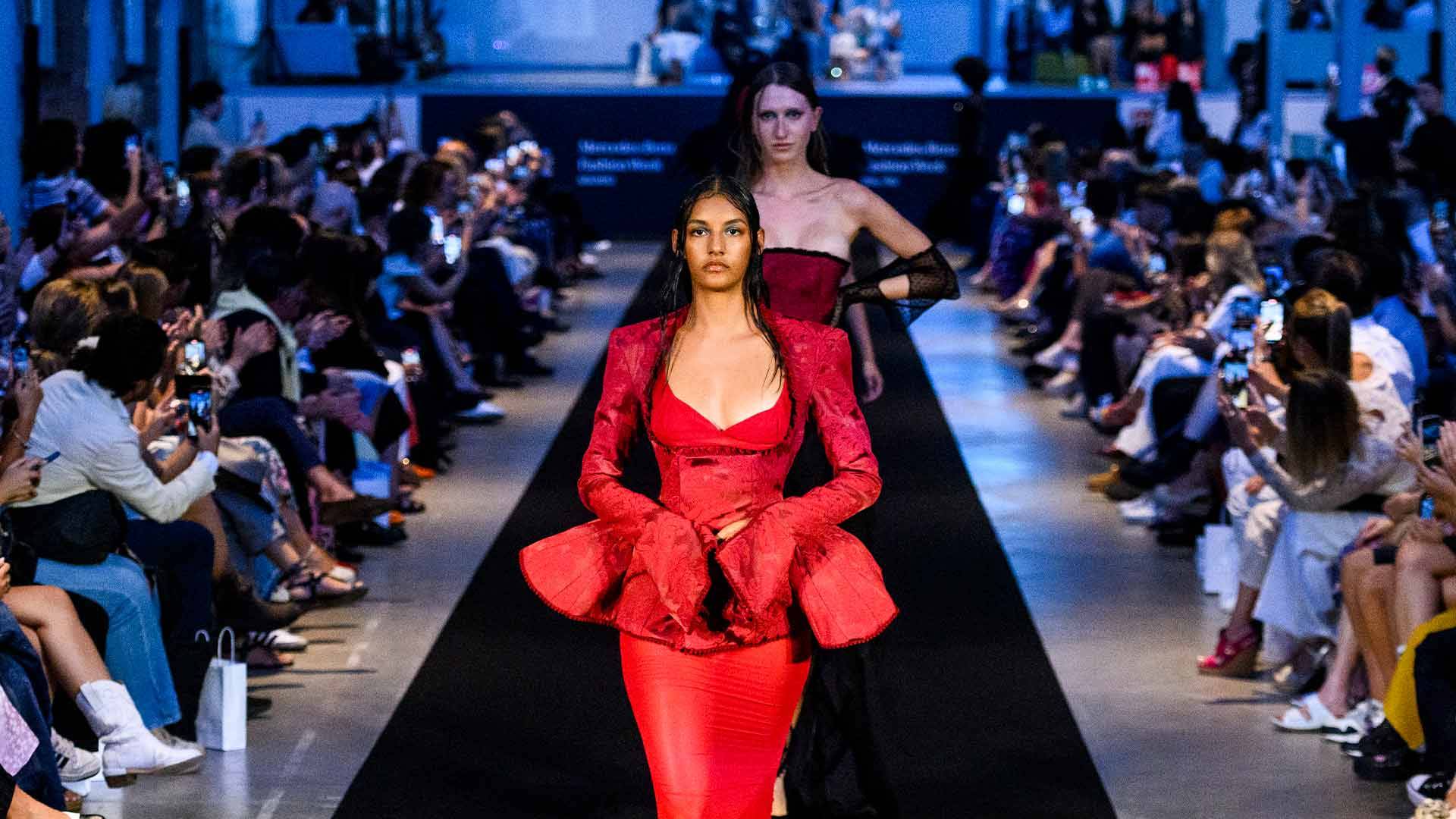 Una pasarela de moda donde las modelos lucen trajes de colores llamativos frente a un público atento.