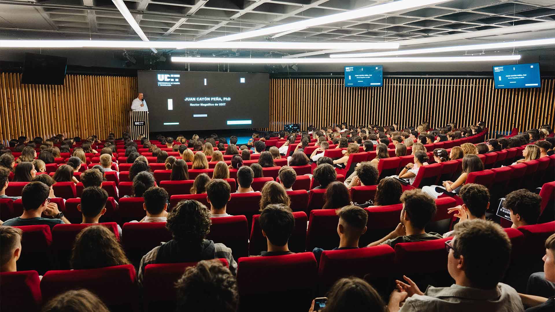 Una sala de conferencias llena de personas prestando atención a un ponente en el escenario.