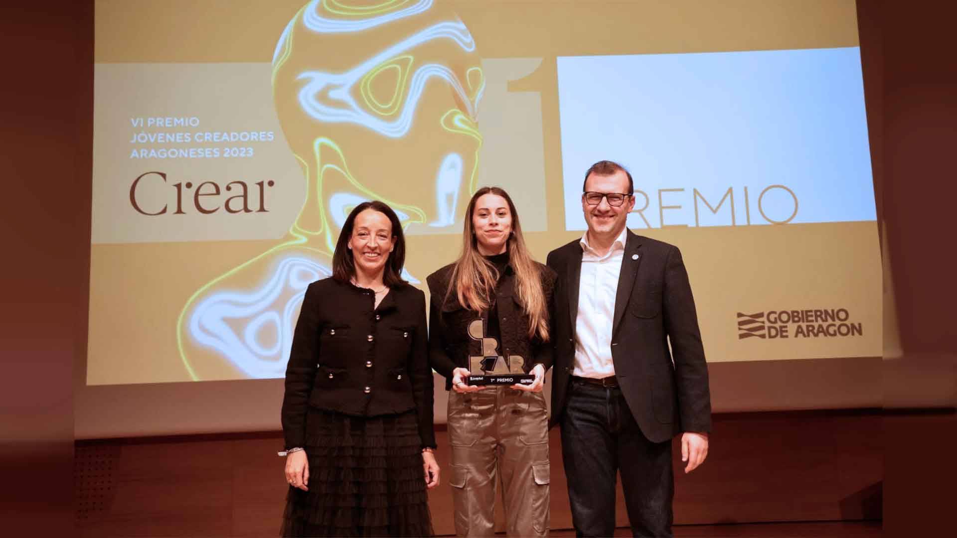 Una entrega de premios con tres personas posando en el escenario, una de ellas sosteniendo un trofeo.