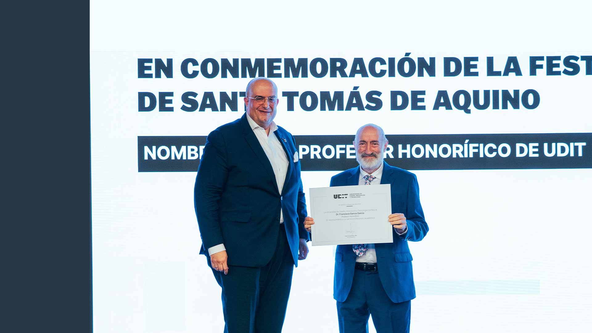 Dos hombres posan juntos mientras uno sostiene un certificado de reconocimiento en un evento conmemorativo.