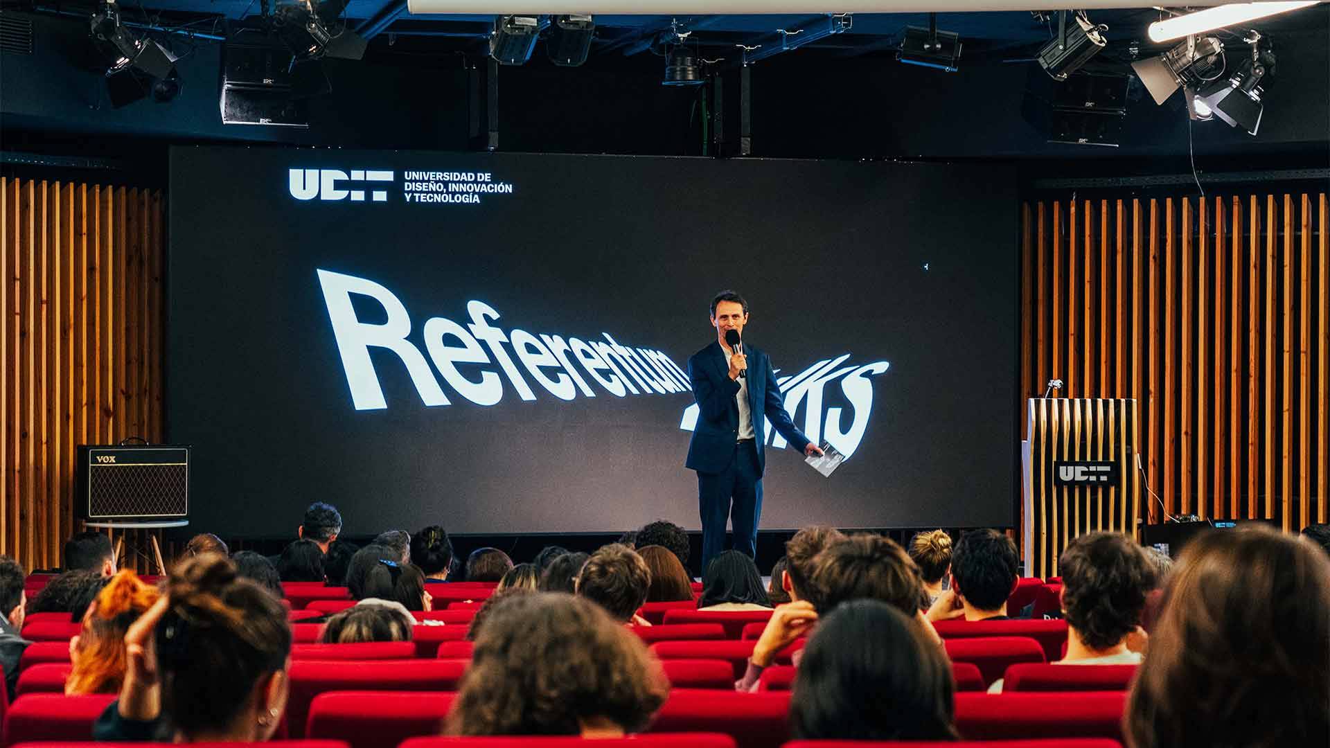 Un presentador habla frente a una audiencia en un evento de la universidad UCT con una pantalla grande detrás que muestra la palabra 'Referentes'.