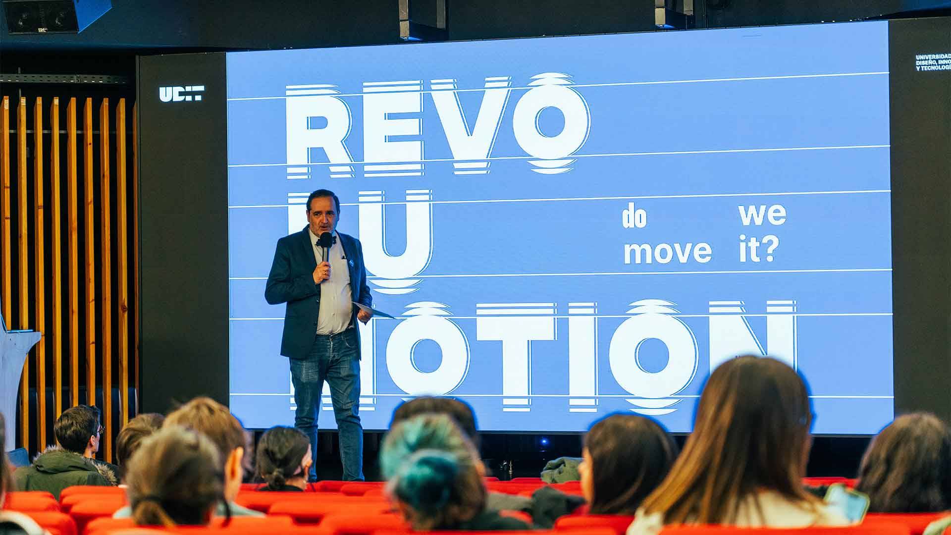 Un presentador habla frente a una pantalla en un evento sobre movimiento y revolución.