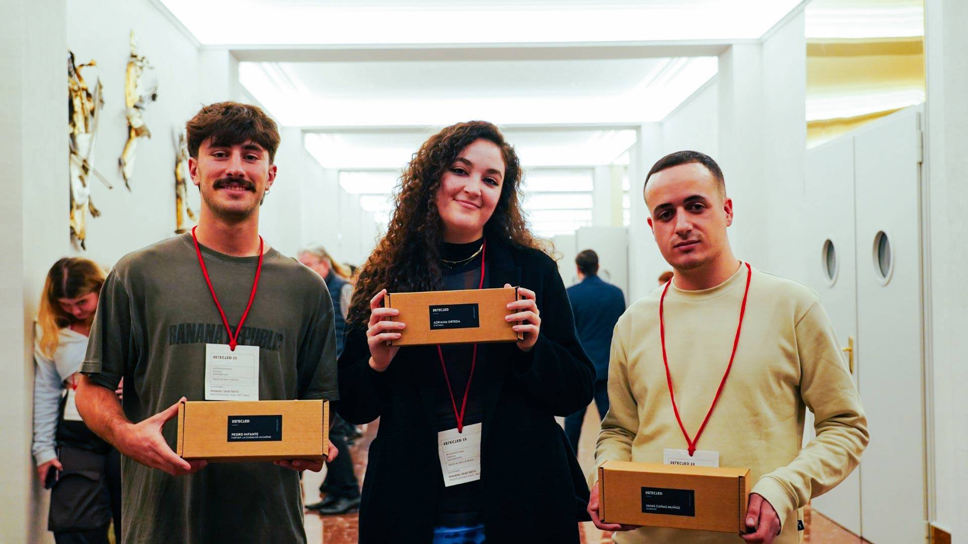 Tres jóvenes sostienen cajas en un evento en un ambiente moderno.