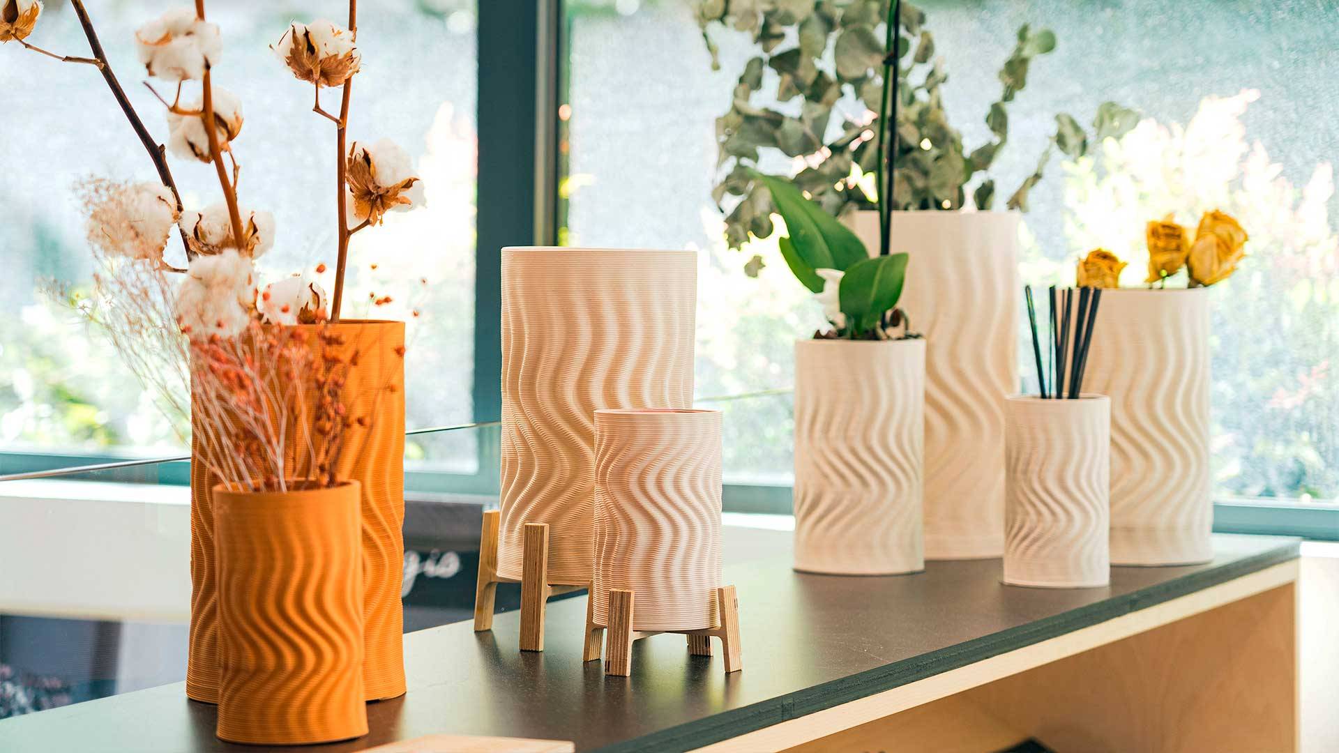 La imagen muestra varios jarrones decorativos con flores y ramas en un ambiente iluminado y moderno.