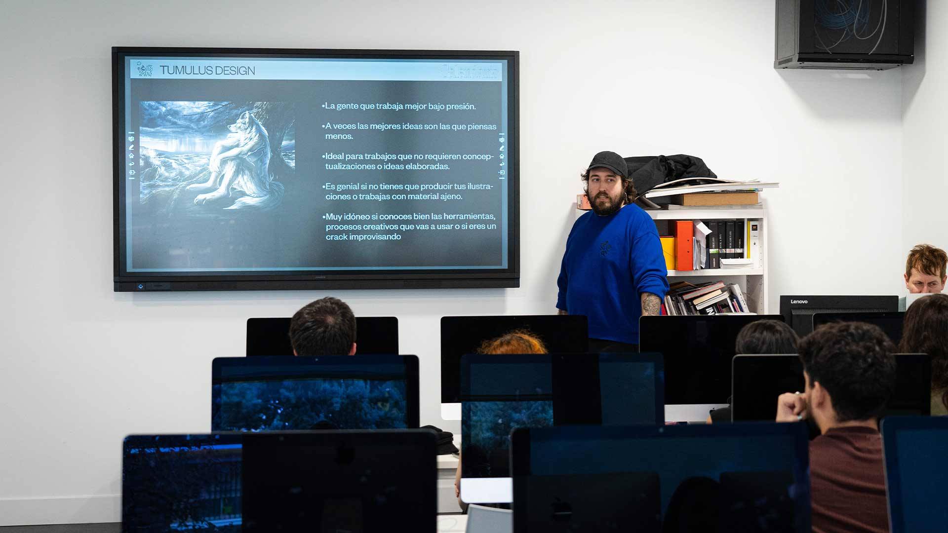 Un instructor presenta una lección sobre diseño mientras los estudiantes lo escuchan en un aula equipada con computadoras.