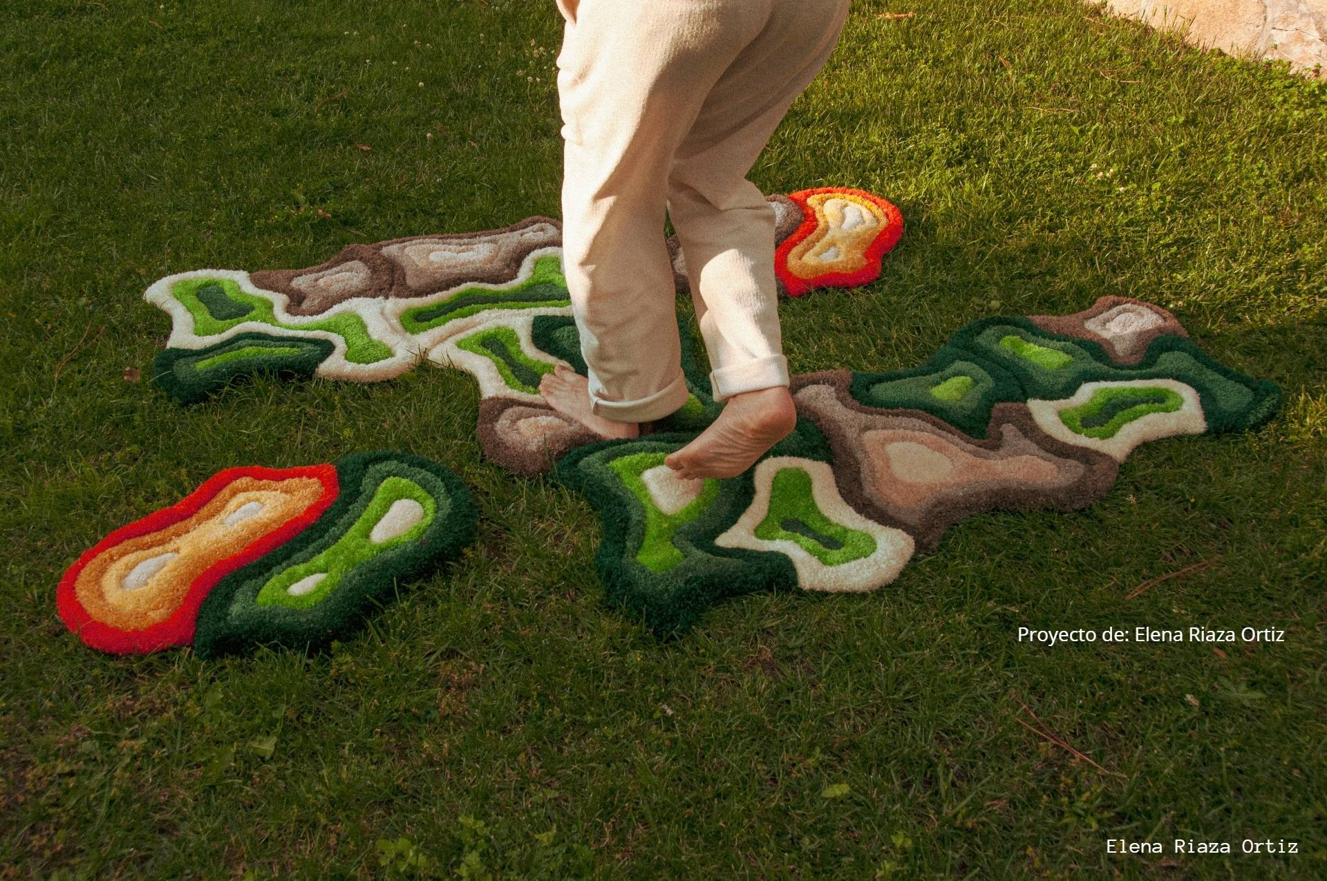 Una persona descalza camina sobre una alfombra de césped en forma de varios colores y formas naturales.
