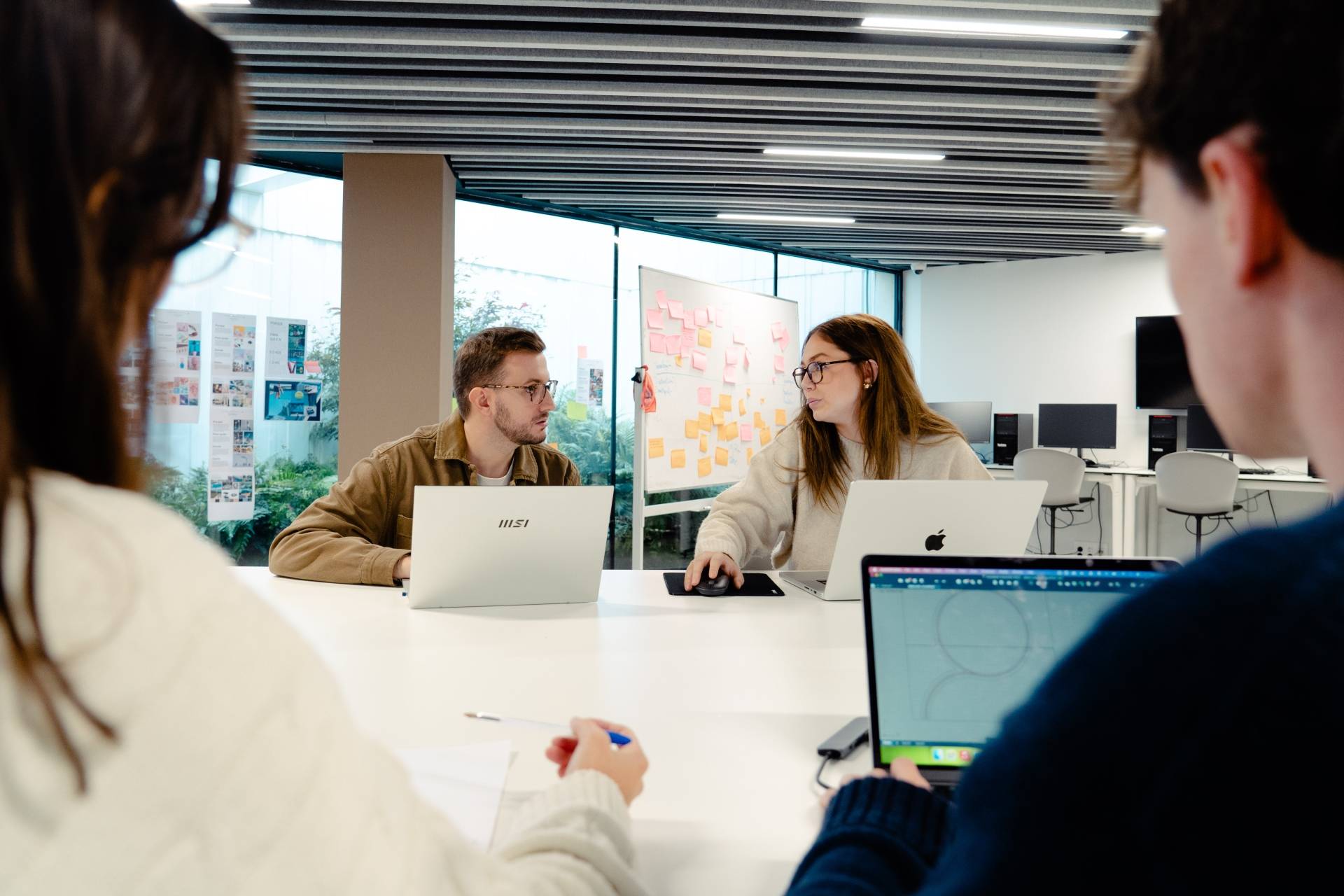 Un grupo de estudiantes trabaja en una mesa colaborando en un proyecto mientras usan laptops.
