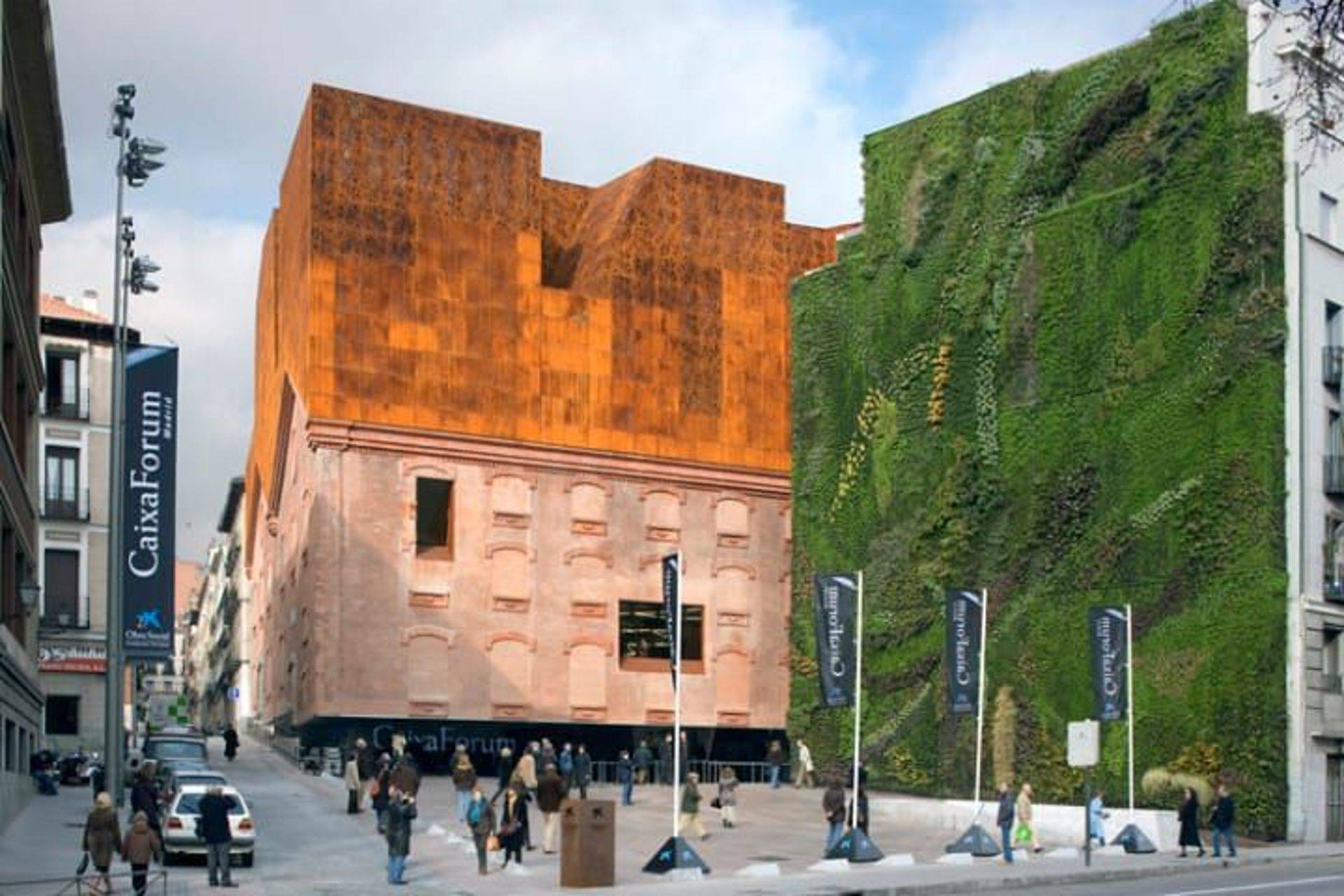 La imagen muestra el edificio del CaixaForum en Madrid, con una fachada contemporánea de metal y vegetación.