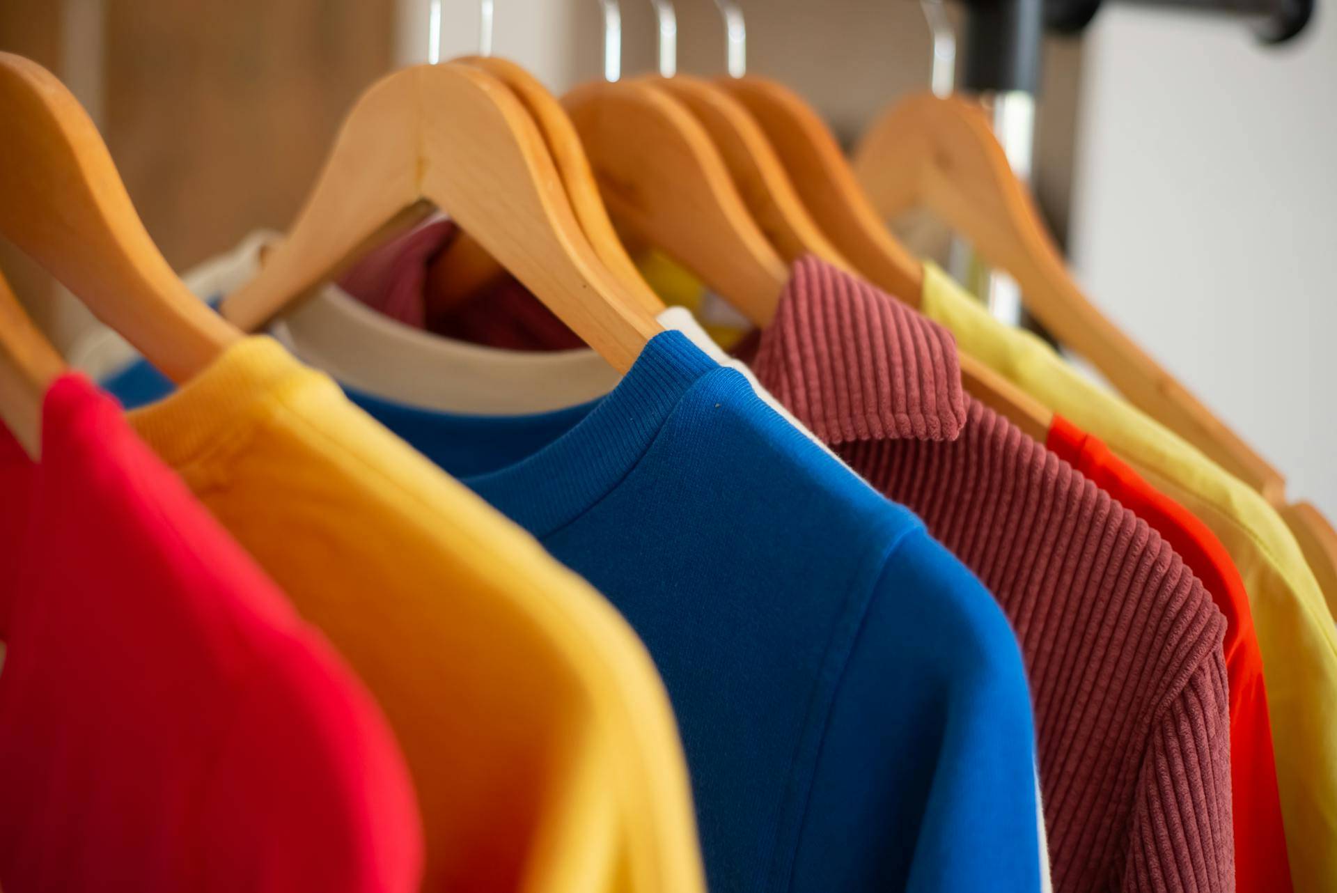 Una fila de camisetas de diferentes colores colgadas en perchas.