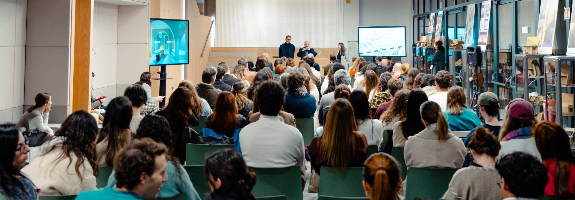 Una audiencia atenta en un evento con presentación en pantallas.