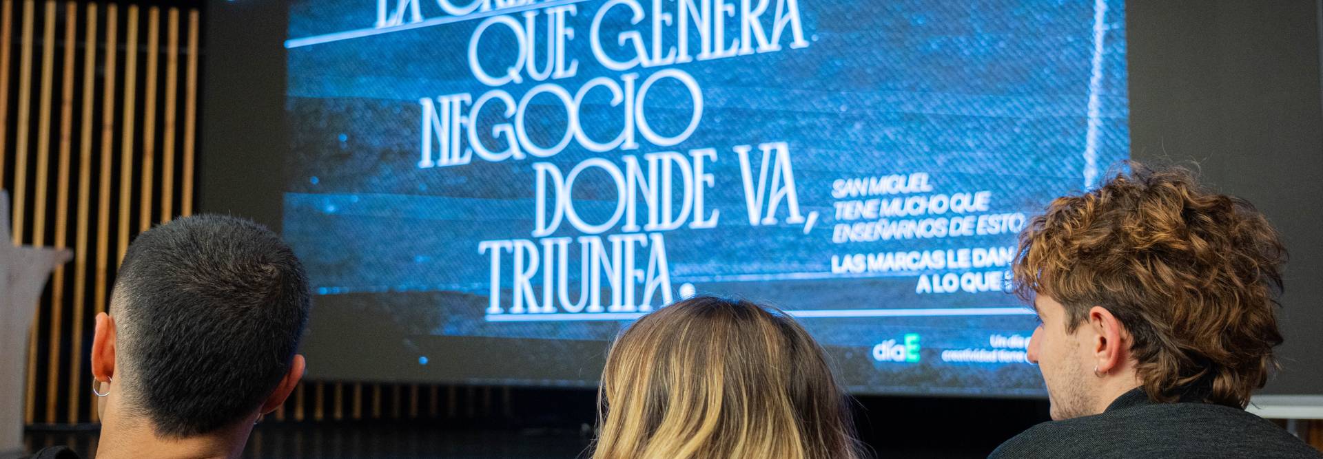 Tres personas observan una presentación en pantalla con un mensaje inspirador sobre el negocio y el éxito.