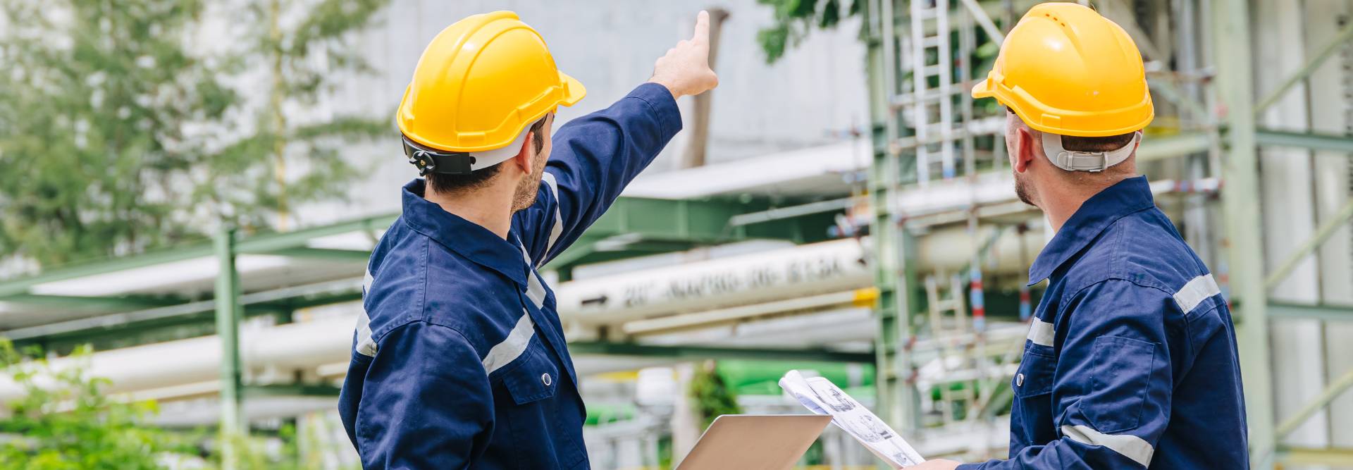 Dos trabajadores con cascos de seguridad observan y señalan una estructura industrial.