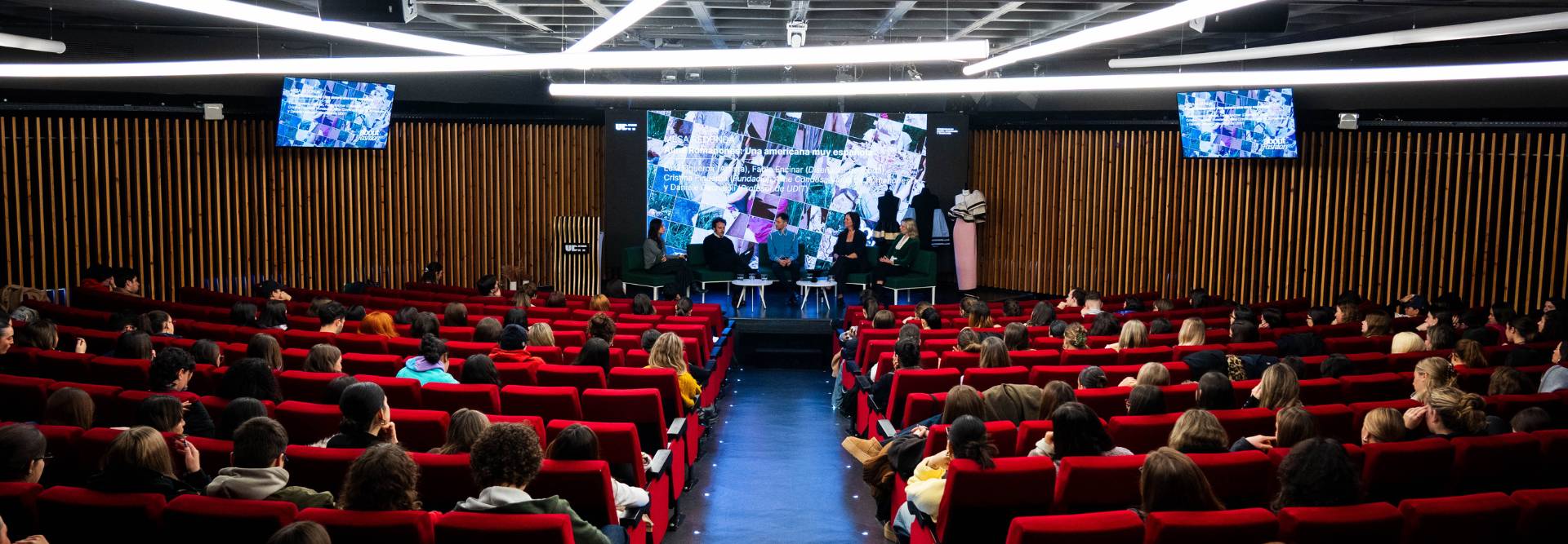Un evento académico con un panel de discusión frente a una audiencia en un auditorio moderno.