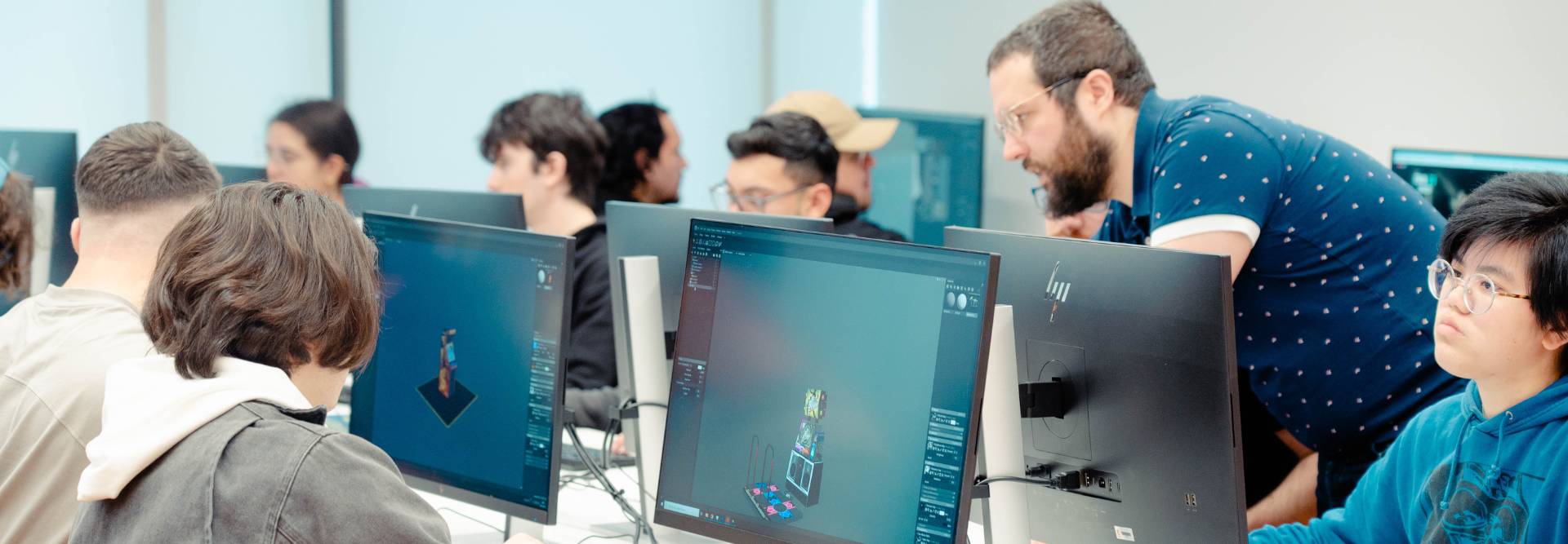 Un grupo de estudiantes trabajando en ordenadores mientras un profesor les guía.