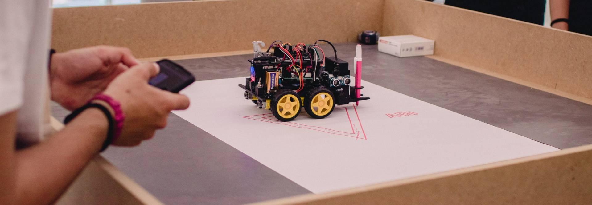 Un robot controlado por un teléfono móvil está dibujando en una hoja de papel en una mesa.
