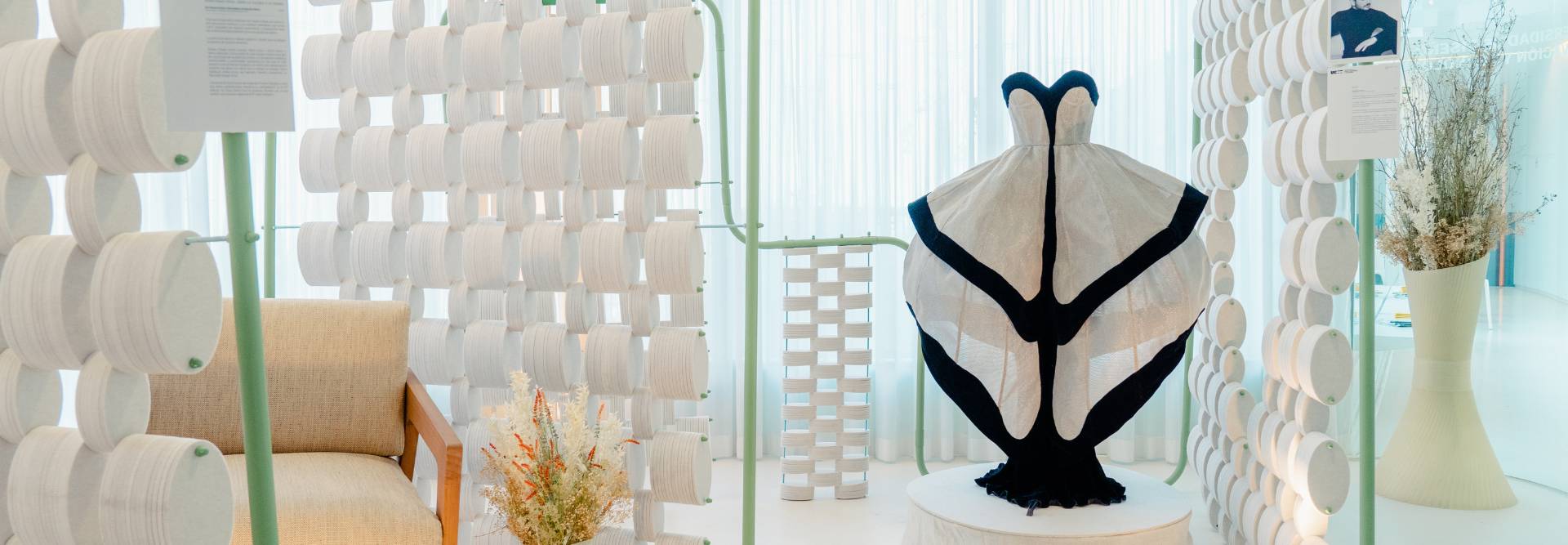 La imagen muestra un vestido de diseño innovador exhibido en un entorno minimalista con elementos decorativos.