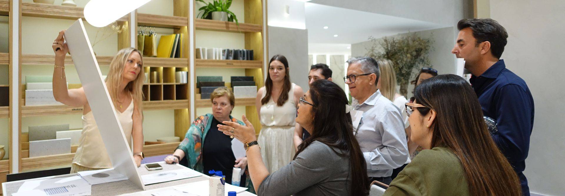Un grupo de personas se reúne en un espacio moderno, donde una mujer está presentando un objeto a los demás.