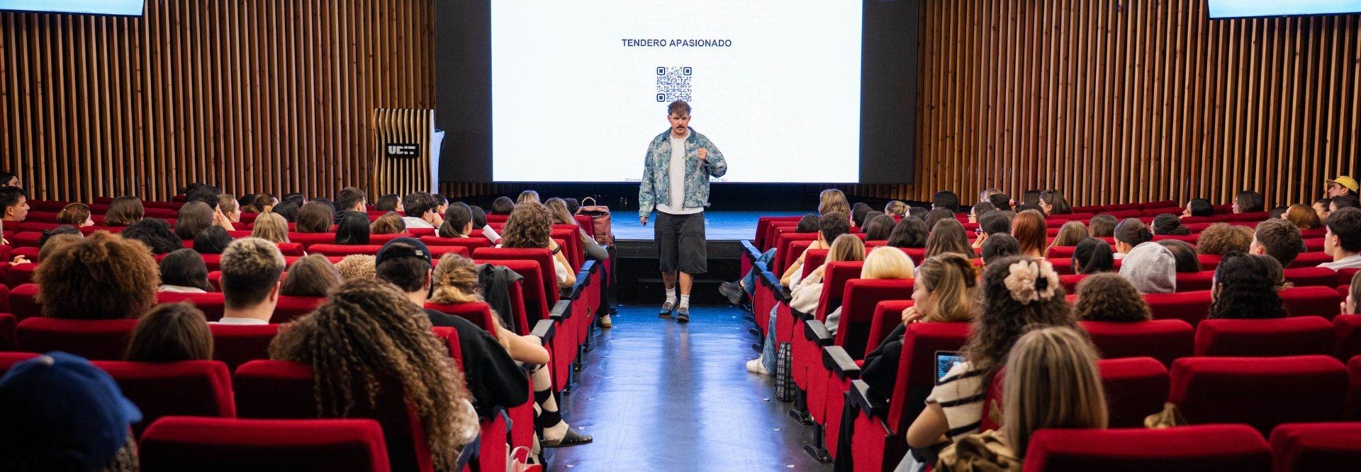 Un orador presenta frente a una gran audiencia en un auditorio moderno.