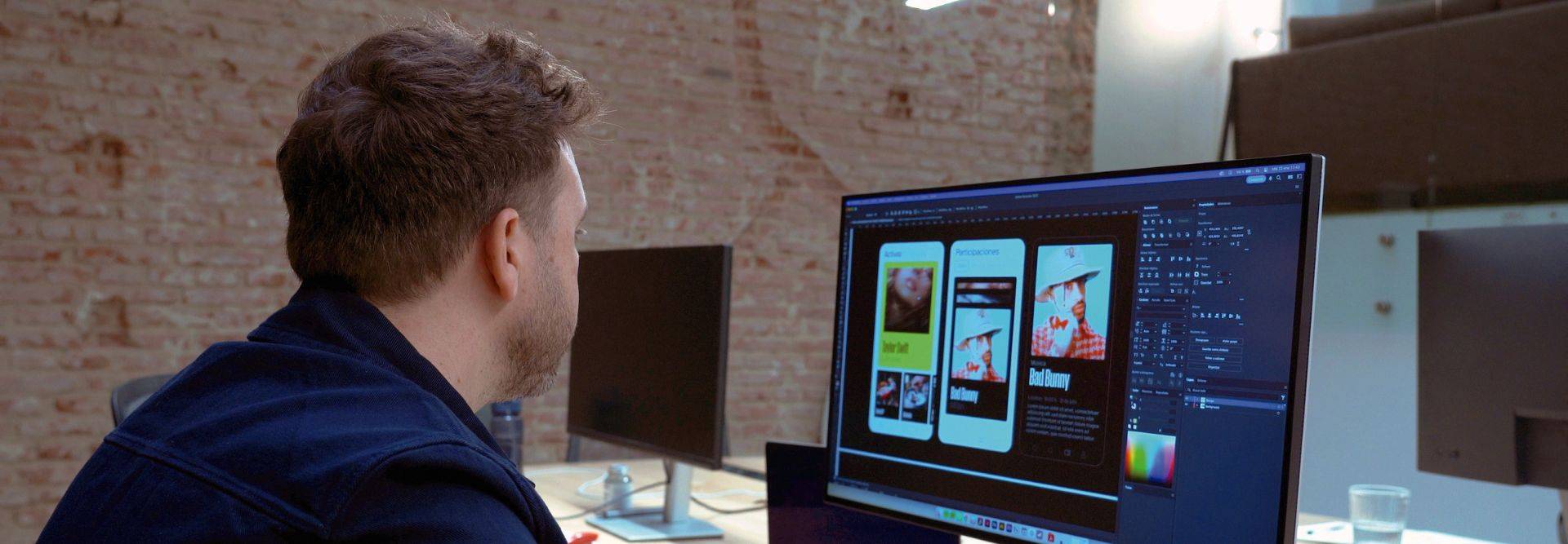 Una persona trabaja en su computadora mientras revisa diseños de aplicaciones móviles.