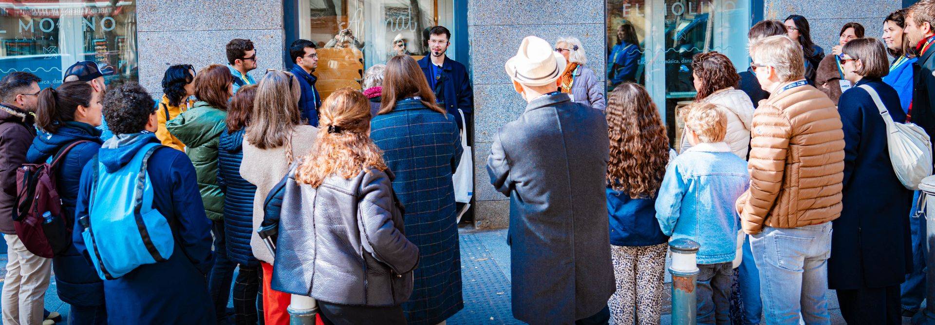 Un grupo de personas observa a un orador en la calle frente a una tienda.