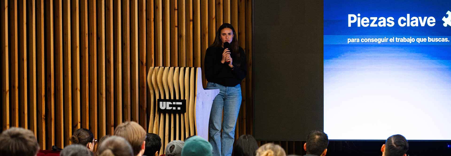Una persona está hablando en una conferencia mientras el público escucha atentamente.
