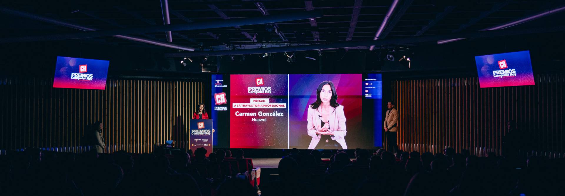 Una presentación en un evento con una ponente y una pantalla que muestra el nombre de Carmen González.