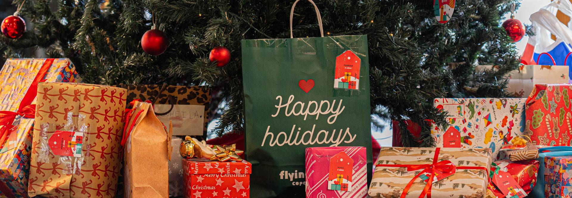La imagen muestra una decoración navideña con regalos envueltos y un árbol de Navidad.