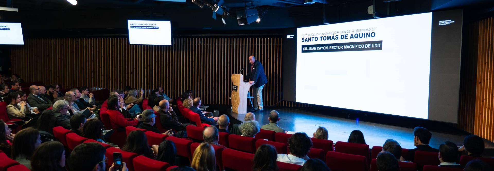 Una conferencia sobre Santo Tomás de Aquino con un orador frente a un público atento.
