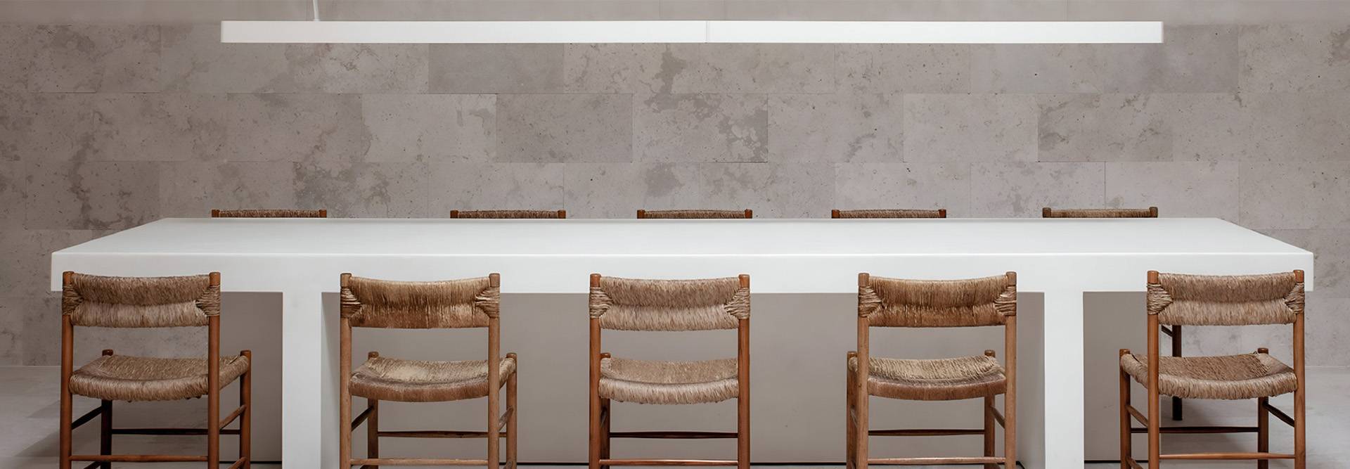 Una mesa blanca con sillas de madera está dispuesta en un entorno minimalista.