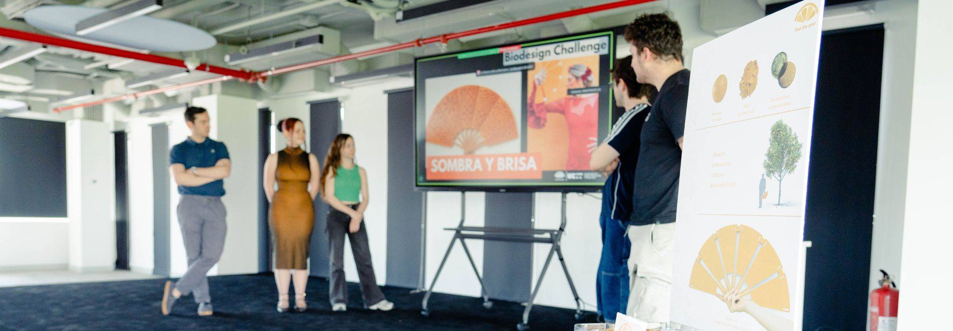 Un grupo de personas presenta un proyecto en una sala equipada con pantalla y gráficos.
