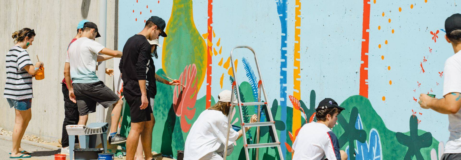 Un grupo de personas pinta un mural colorido en una pared exterior.