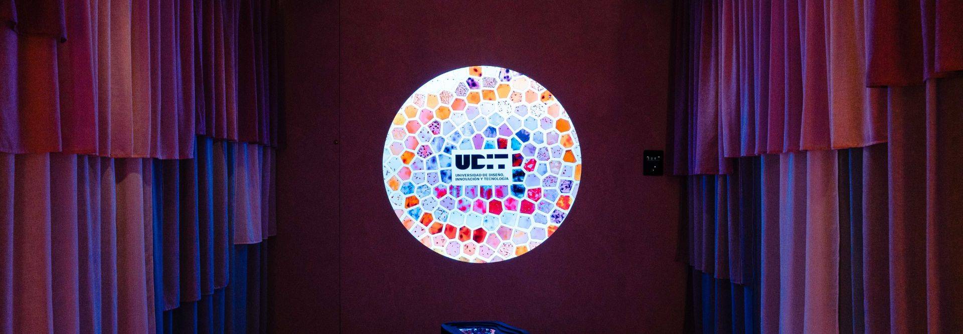 Una habitación con cortinas de colores y una ventana circular iluminada con mosaicos de colores que contiene un logo.