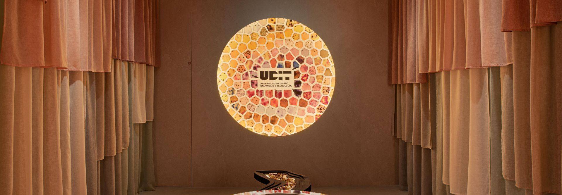 La imagen muestra un ambiente decorativo con un mural circular colorido y cortinas en tonos cálidos.