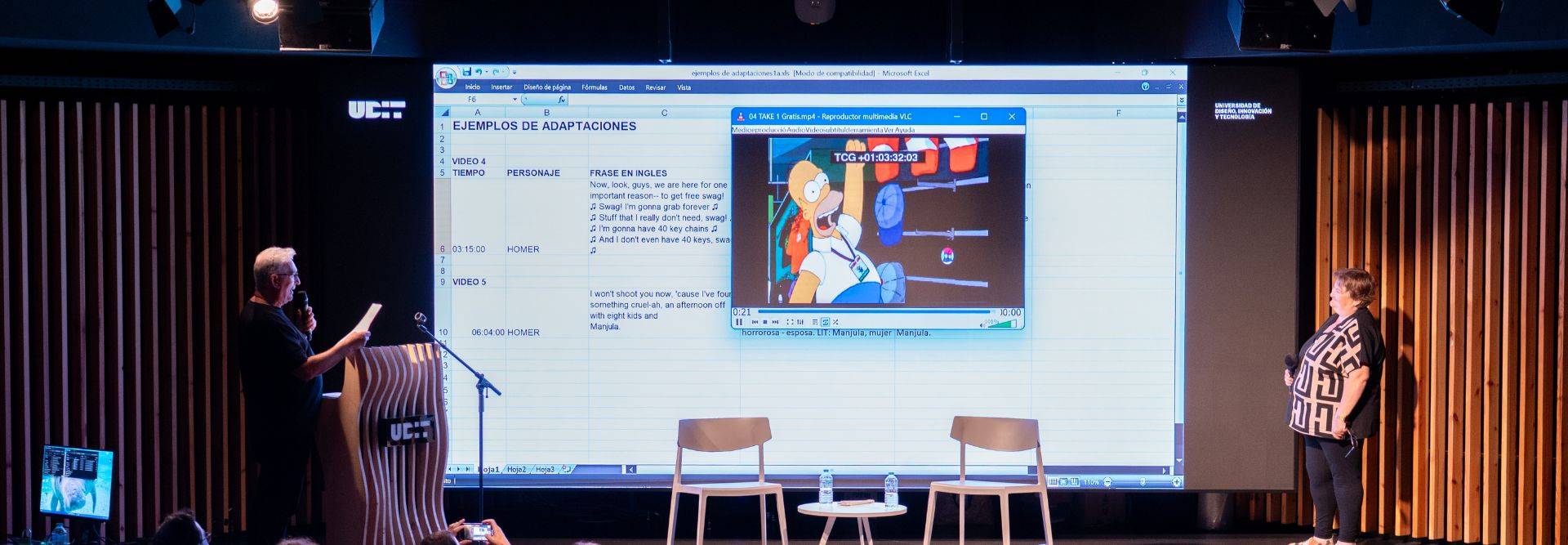 Una presentación en un escenario con una proyección de un video y dos personas en el micrófono.
