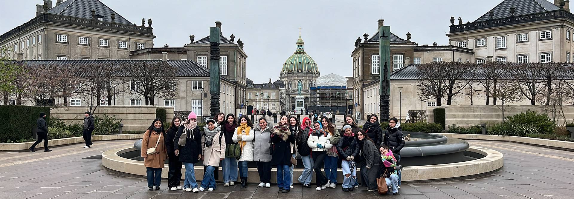 Un grupo de personas posando frente a un edificio con cúpula en un día nublado.