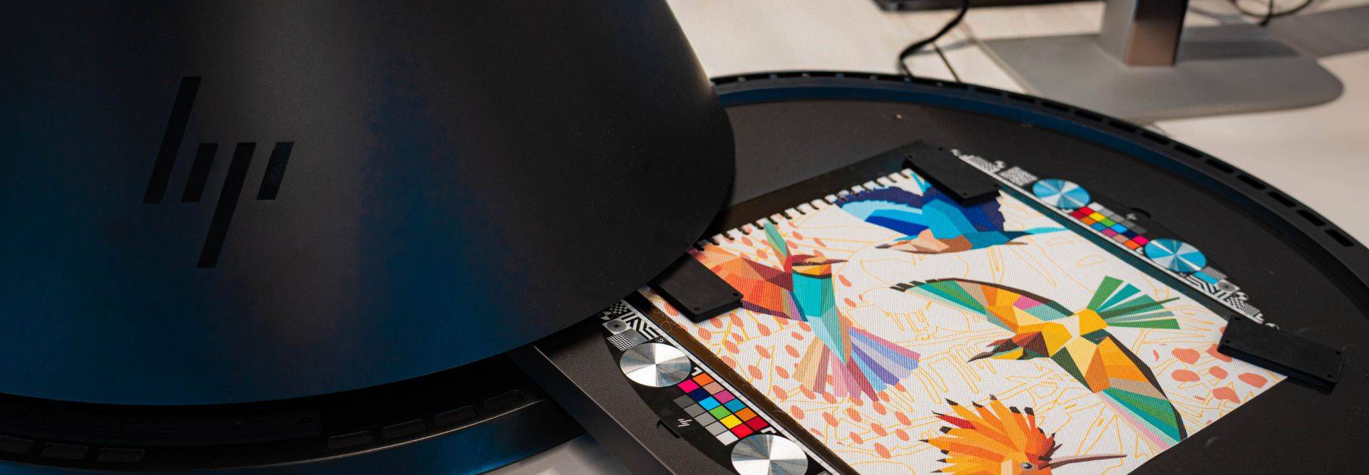 La imagen muestra un escáner HP con una obra artística colorida sobre la mesa.