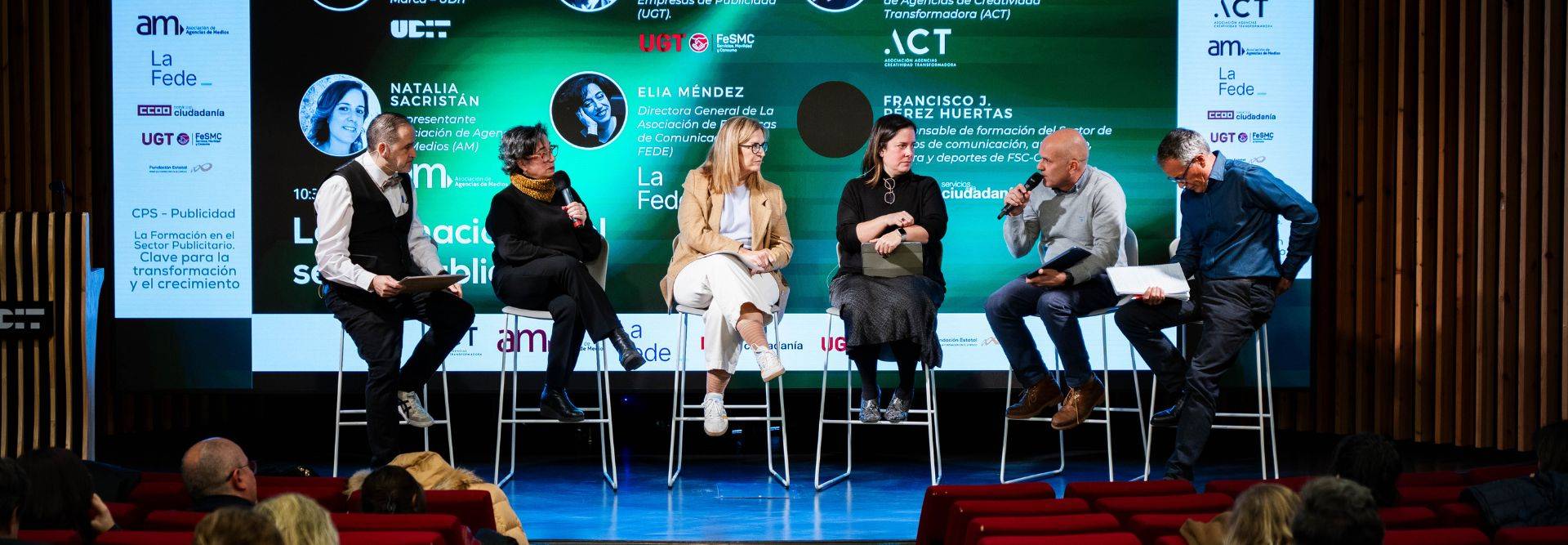 Un panel de discusión con varios presentadores en un escenario.