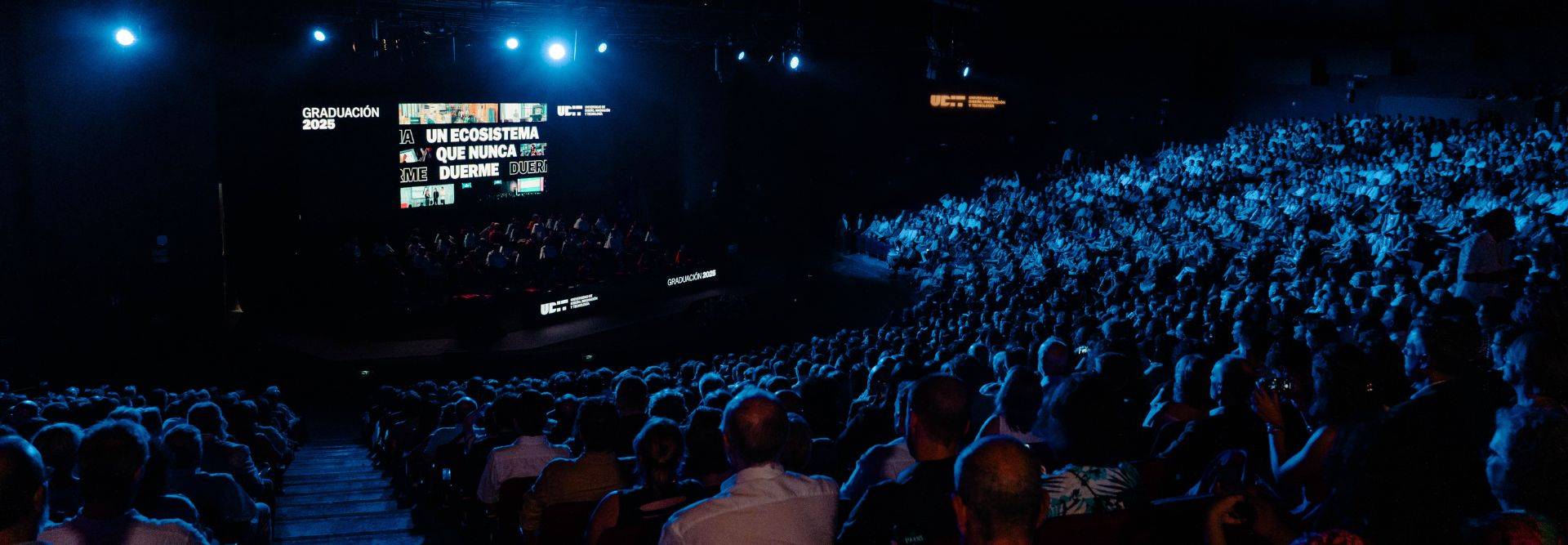 Una gran multitud asiste a un evento en un escenario iluminado con luces azules.