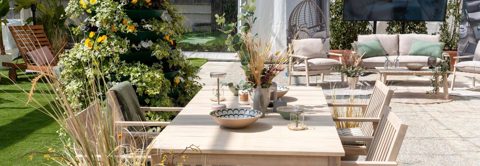 Un elegante espacio al aire libre con una mesa de madera rodeada de sillas y decoraciones vegetales.
